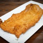 A piece of fried fish on a white plate.