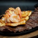A plate with steak, shrimp and potatoes on it.