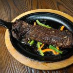 A steak in a skillet on a wooden table.