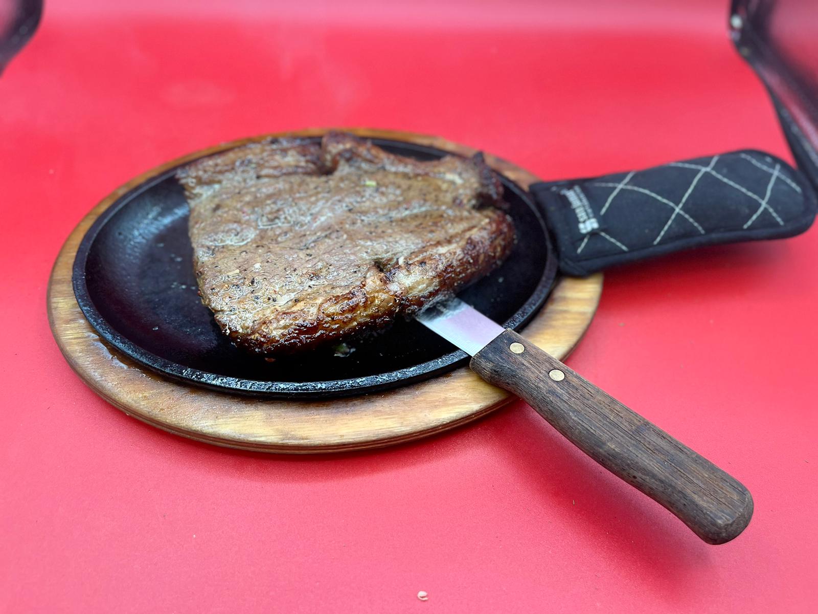 A steak in a pan with a knife on top.