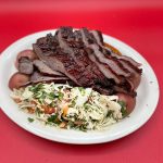 A plate of ribs and coleslaw on a red background.