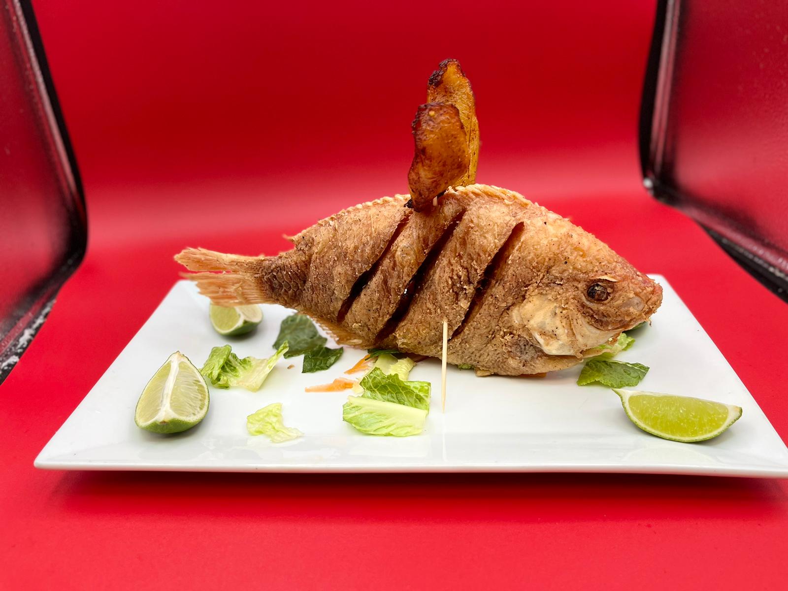 A fried fish on a plate with lime wedges.