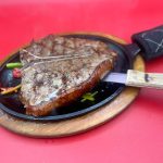 A steak in a pan with a knife on it.