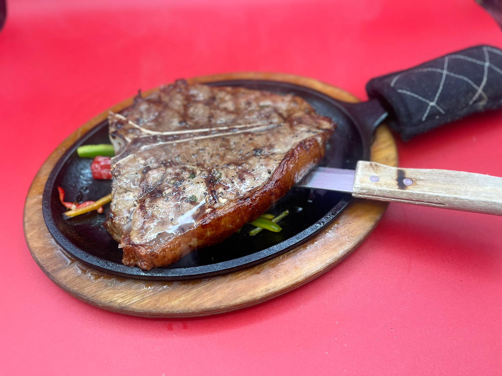 A steak in a pan with a knife on it.