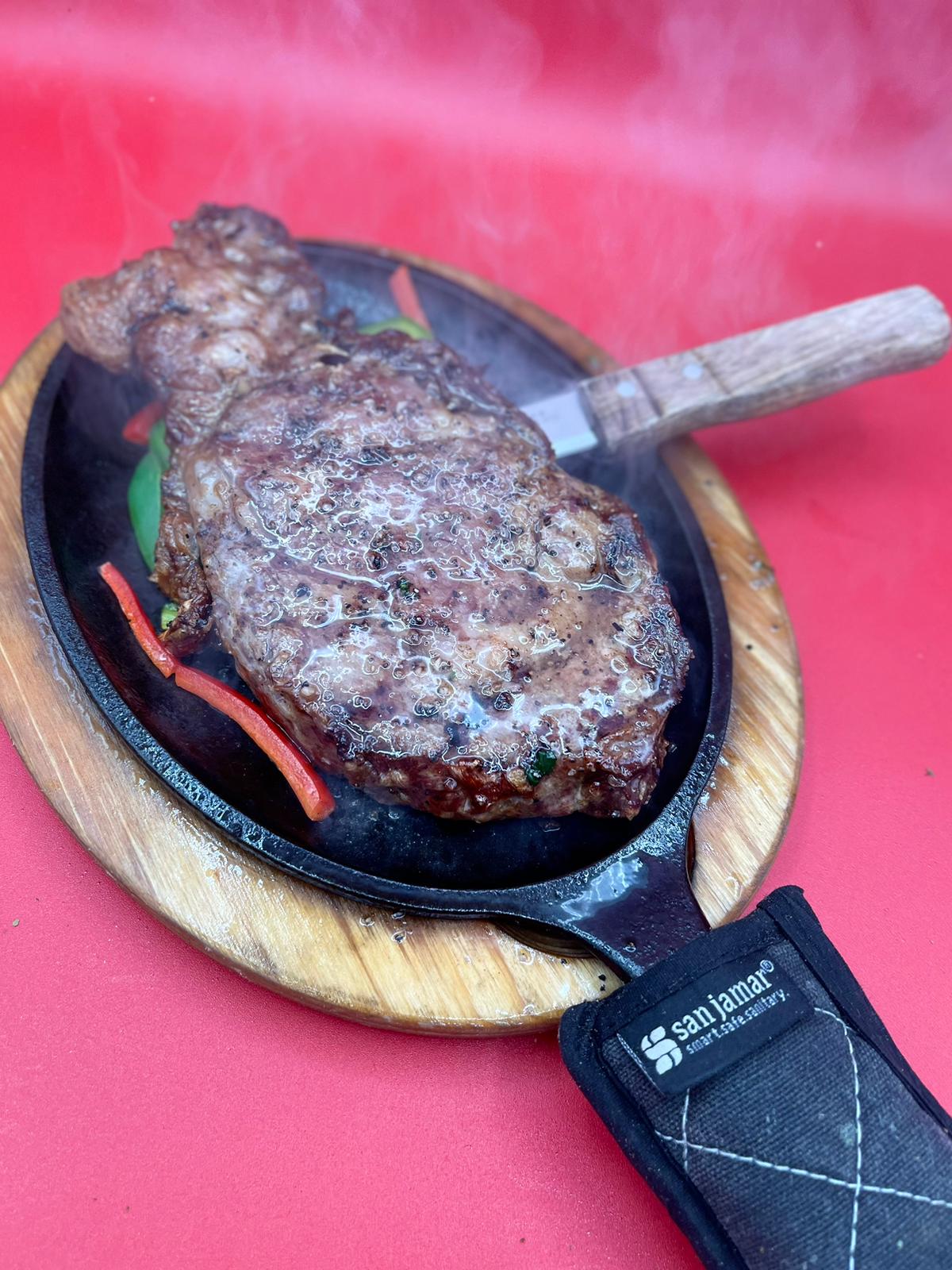 A steak is being cooked in a skillet on a red table.