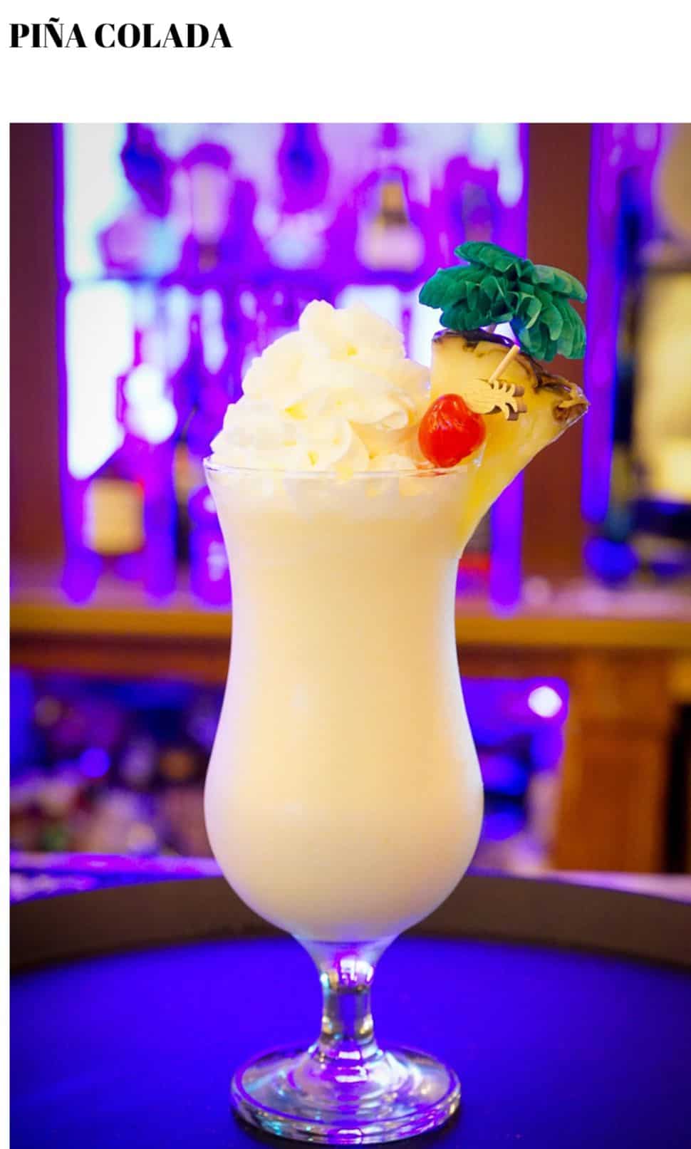 A glass of white liquid with a pineapple and a cherry on top.