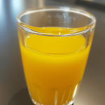 Sideview of orange juice on a transparent cup on top of a table.